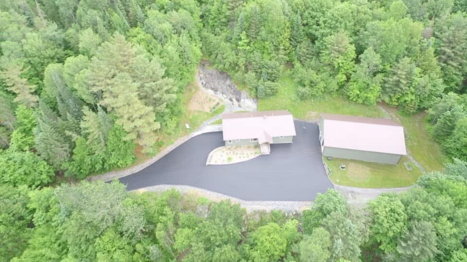 Overhead of a paved pad and driveway around a house in the woods