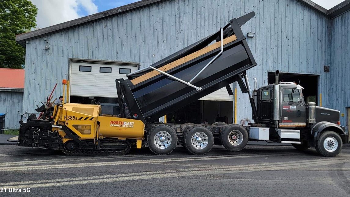 Northeast Paving dump truck feeding a branded yellow paver