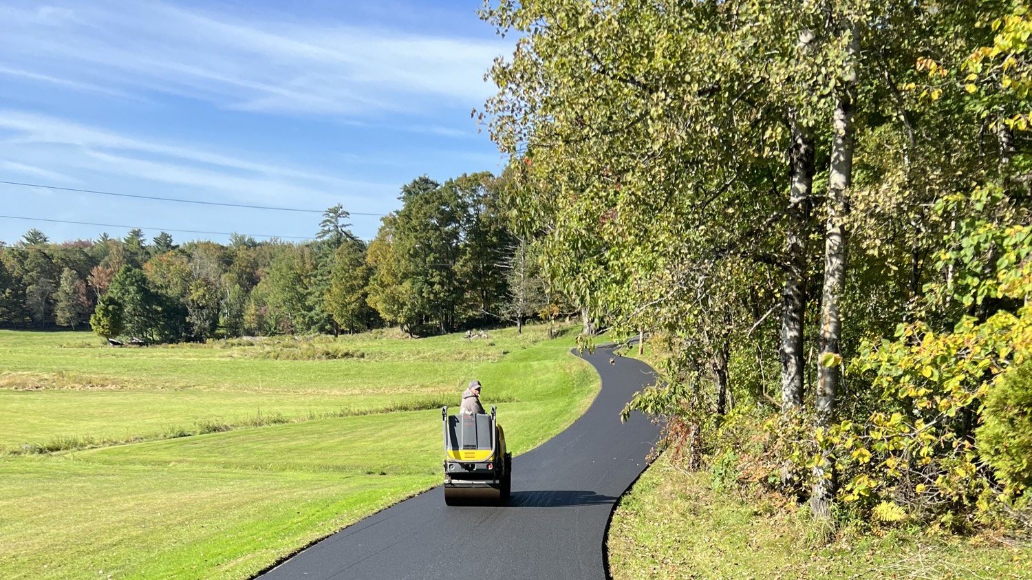 Roller compacting a long winding blacktop driveway through a Vermont hayfield